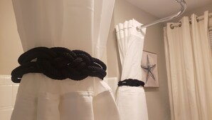 Un baño con cortinas de ducha blancas, un perchero metálico y una decoración de estrella de mar en la pared.