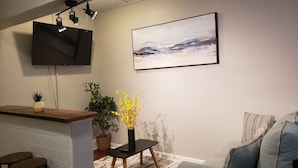 Una sala de estar moderna con un sofá gris, una mesa de centro de madera, un televisor montado en la pared y un cuadro sobre el sofá.