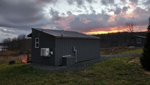 A small, dark-colored metal building with a sloped roof, an air conditioning unit, and a small window.