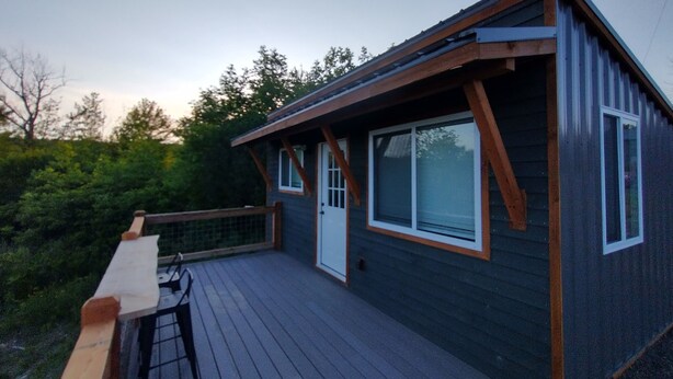 A small, dark-colored cabin with a wooden deck and a white door.