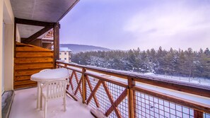 A balcony with a wooden railing, a white plastic chair, and a view of a snowy landscape with trees and a building in the distance.