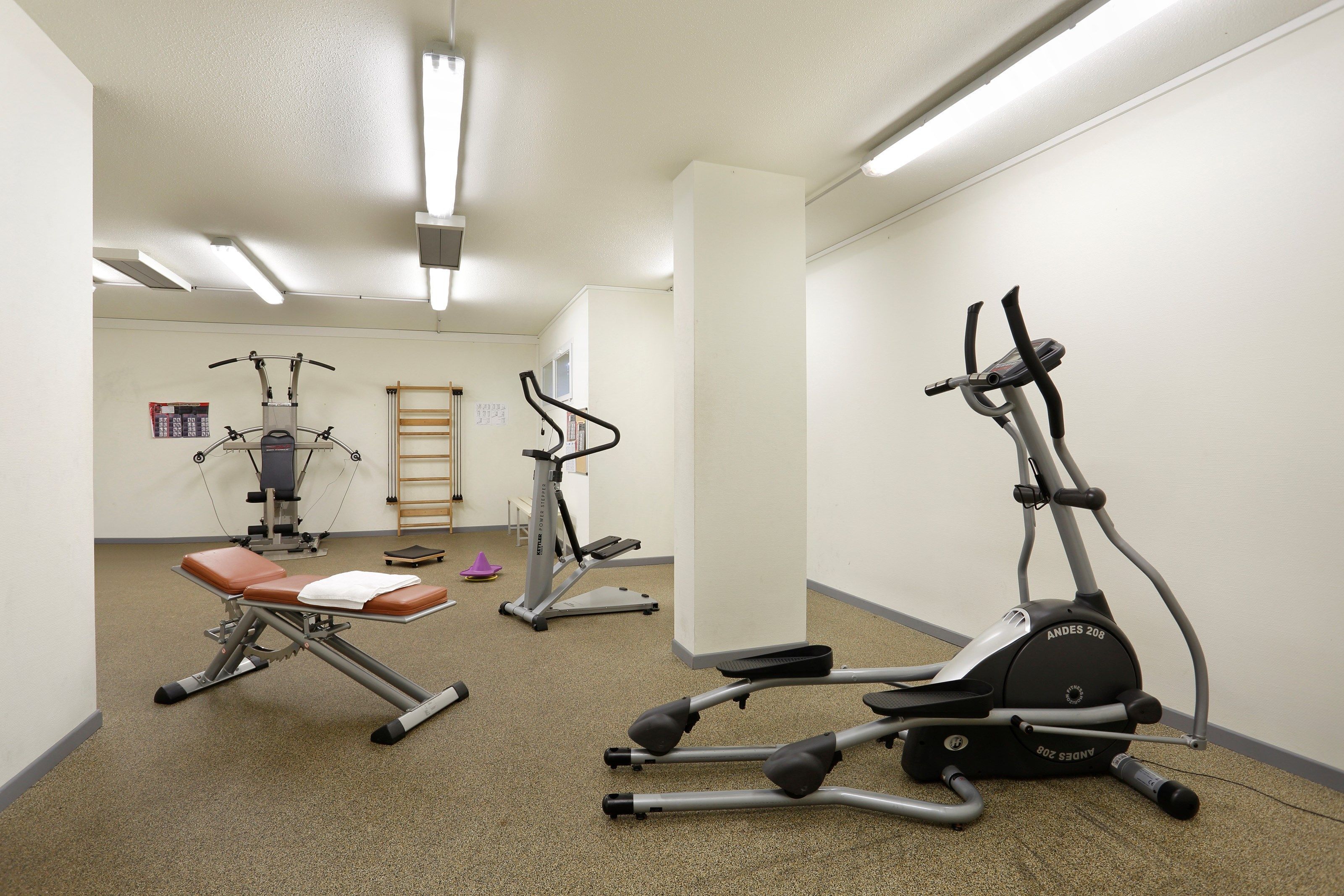 A fitness room with various exercise equipment, including a stationary bike, elliptical, and weight machine.