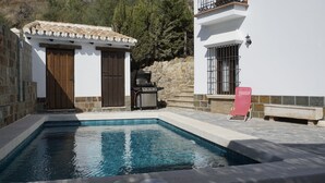 A swimming pool with a stone border, a barbecue grill, and a stone wall. - Rural House The Promise (Malaga)