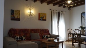 A living room with a sofa, a coffee table, and a dining area with chairs and a table. There is a wall-mounted light fixture and artwork on the wall. - Rural House The Promise (Malaga)