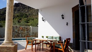 A patio with a table and chairs, a white wall with two wall-mounted lights, and a view of a mountainous landscape. - Rural House The Promise (Malaga)