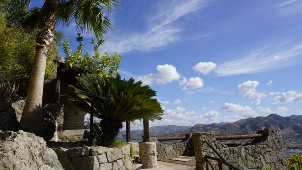 A stone structure with a stone wall and a wooden railing, surrounded by greenery and a clear sky. - Rural House The Promise (Malaga)