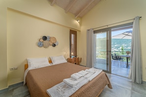 A bedroom with a large bed, a nightstand, a wall decoration, and a view of the outdoors.