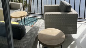 Ein Balkon mit Korbmöbeln, einem kleinen Tisch und Blick auf einen See und Gebäude.