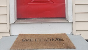 A red door with a 'WELCOME' mat in front.