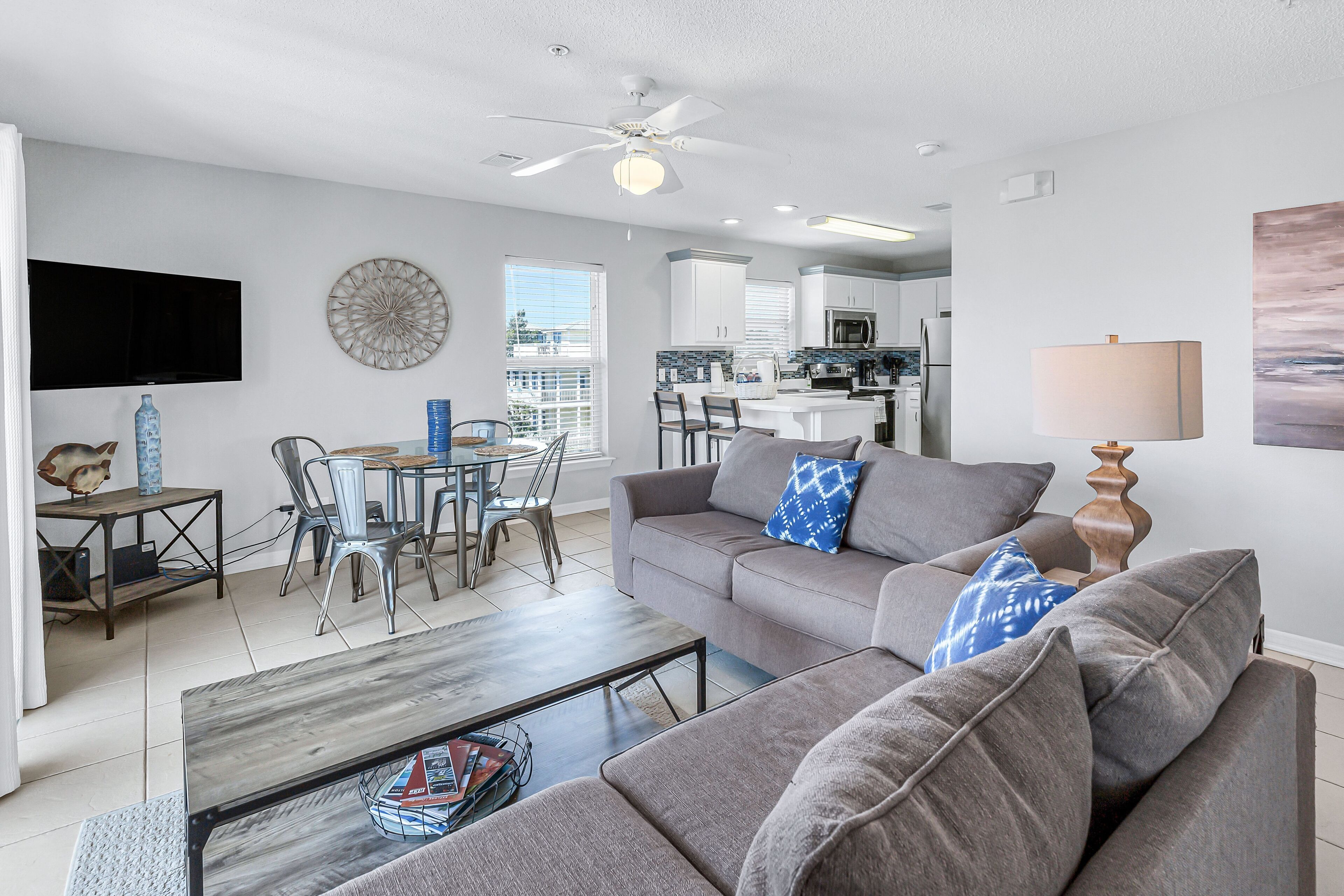 A modern living room with a gray sofa, a coffee table, and a dining area with metal chairs.