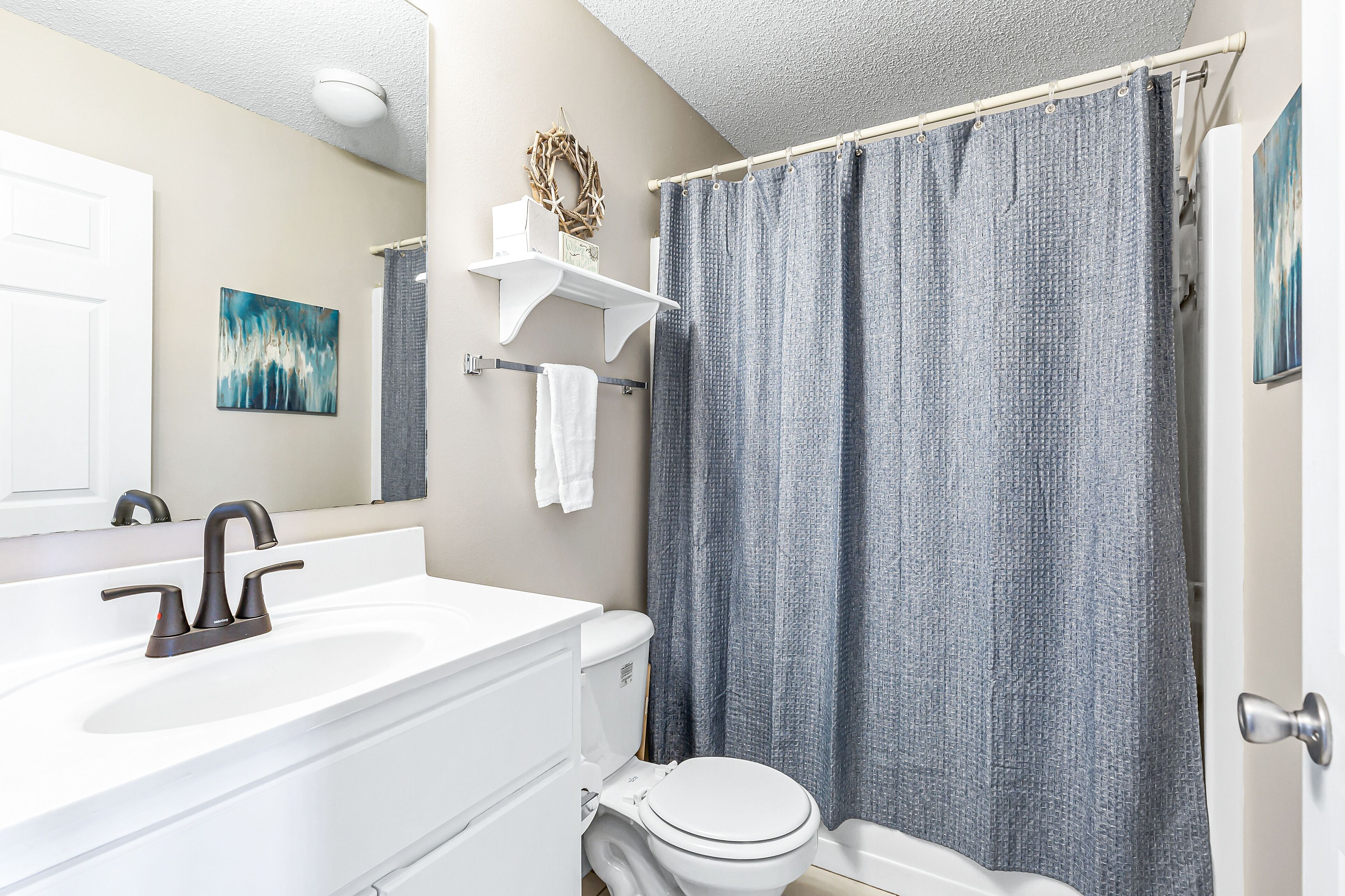 A bathroom with a white sink, a modern faucet, a toilet, and a shower curtain.