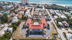 Vue aérienne d’un quartier résidentiel situé sur la côte, avec de nombreux immeubles, dont un hôtel imposant doté d’un toit rouge et d’une piscine.