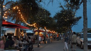 Un espace extérieur aménagé pour les repas, avec des tables, des chaises, des guirlandes lumineuses et des parasols.