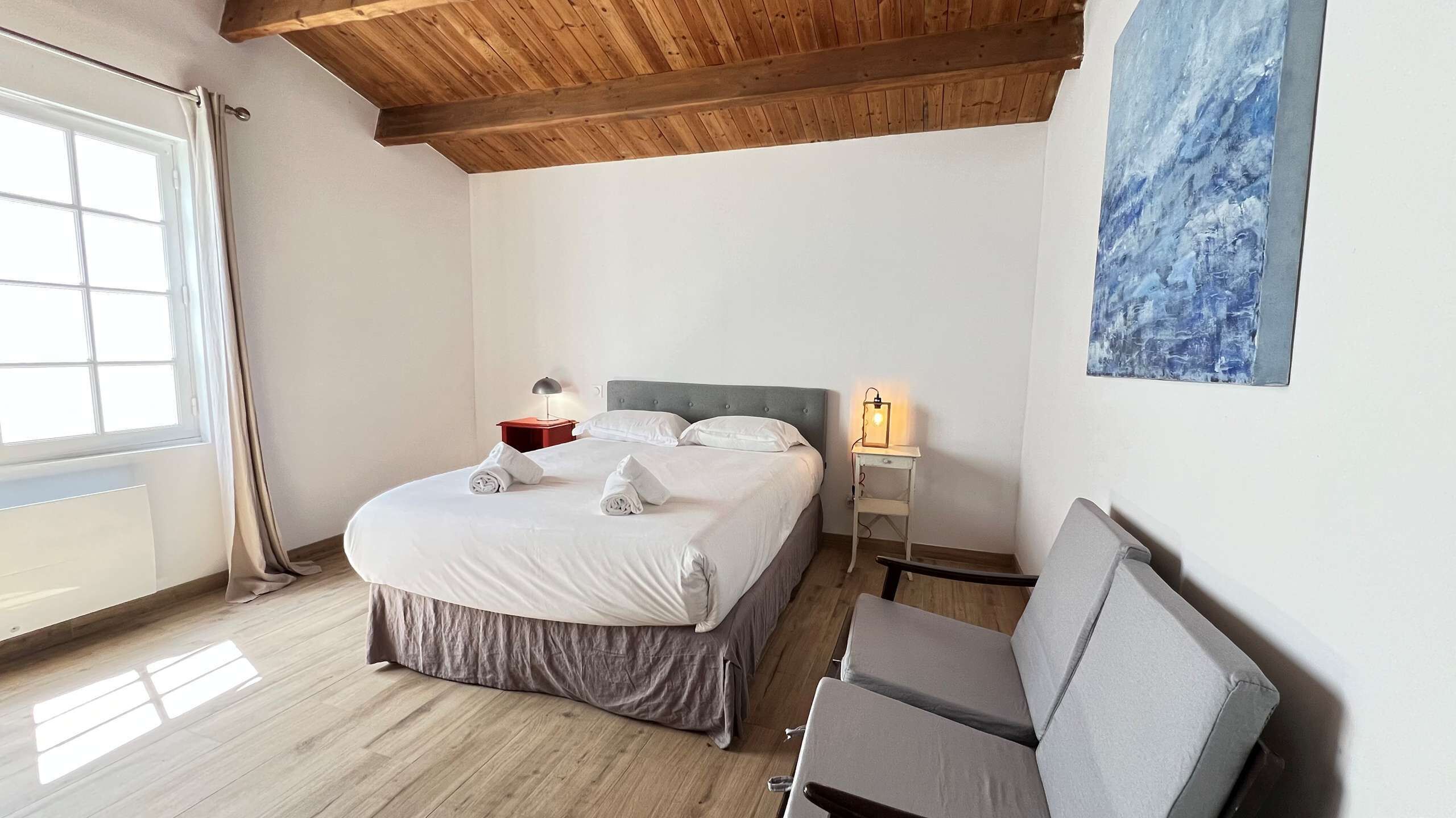 A neatly arranged bedroom with a bed, bedside table, lamp, and a chair.