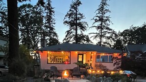 A house with a fire pit and outdoor seating, surrounded by large rocks and trees.