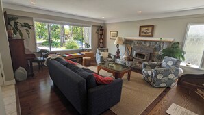 A living room with a sofa, armchair, coffee table, fireplace, bookshelf, and large windows.