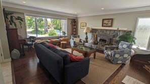 A living room with a sofa, armchair, coffee table, fireplace, bookshelf, and large windows.