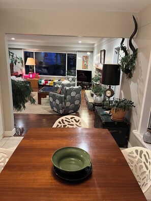 A living room with a wooden dining table, sofas, a television, and decorative plants.