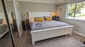 A bedroom with a white bed, a window with a view, a bedside table, and a lamp.