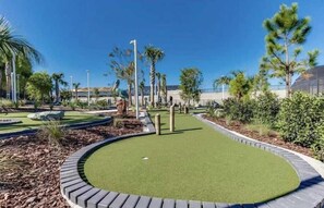 Pienoisgolfkenttä, jossa on vihreä lyöntialue, ja jota ympäröivät kauniit puutarhat ja palmu­puut.
