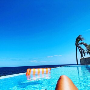 A clear blue sky, a swimming pool with a striped float, and a palm tree.
