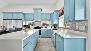 Una cocina moderna con armarios azul claro, electrodomésticos de acero inoxidable y una isla central.