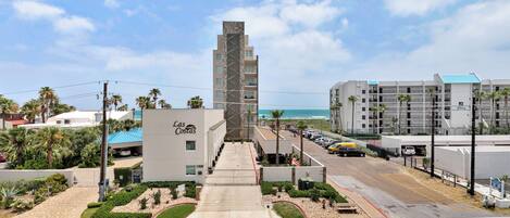 A hotel named "Las Costas" with a central tower, a parking lot, and a view of the beach.