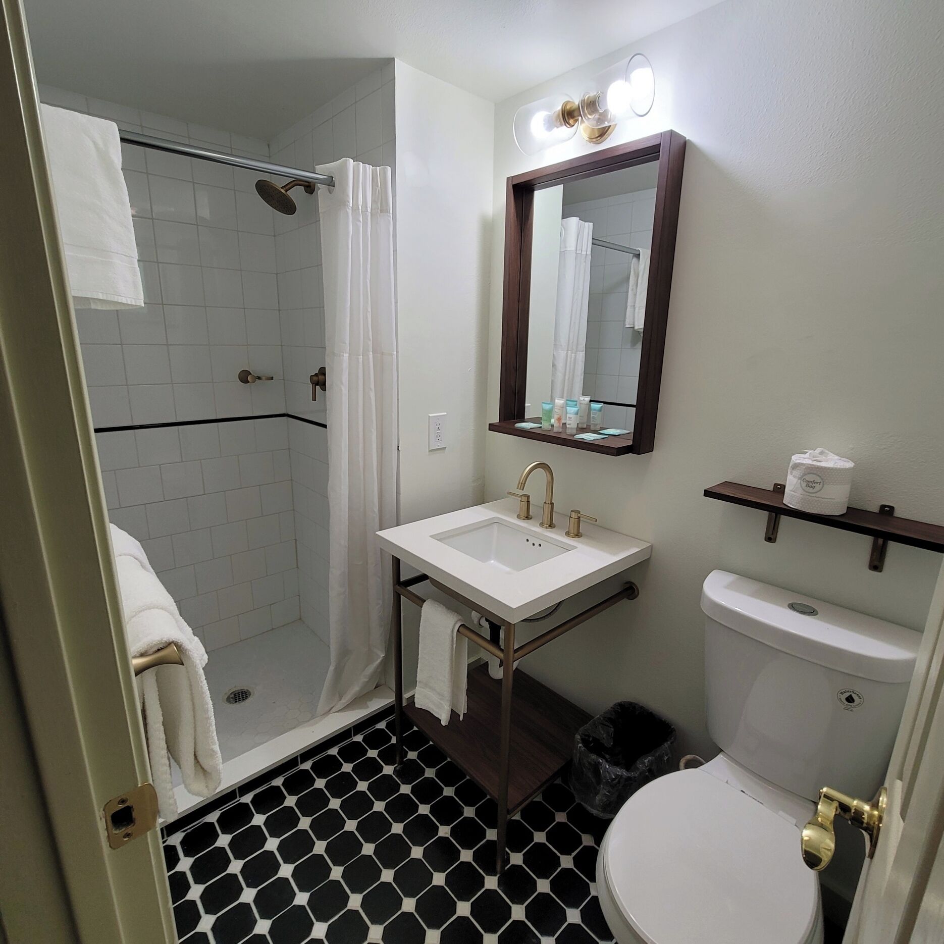 A bathroom with a shower, toilet, sink, and a mirror with lights.