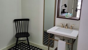 A bathroom with a black and white hexagonal tile floor, a white sink with gold fixtures, a black chair, and a large mirror. - Ski Mountain Lodge (Gatlinburg)