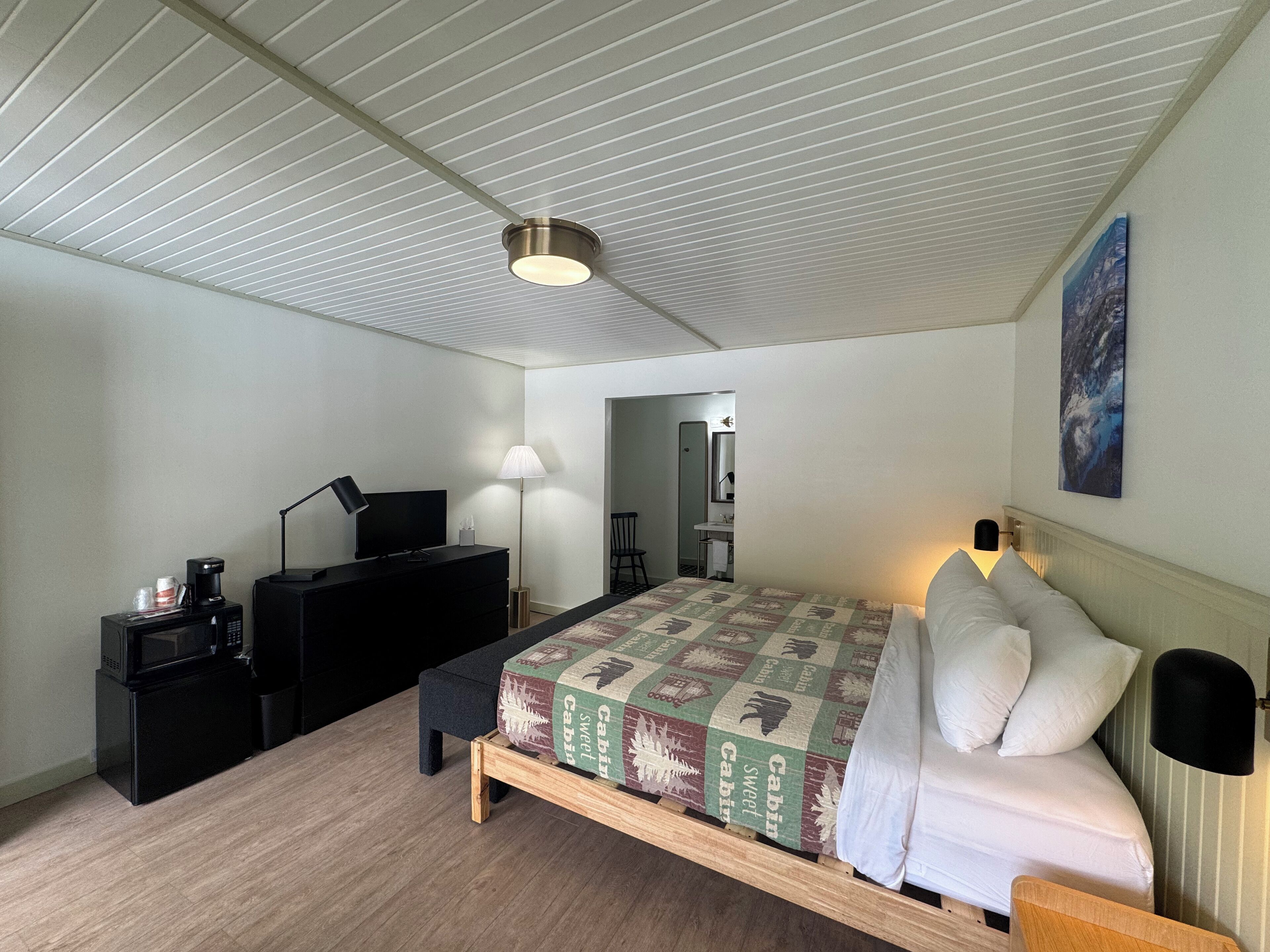 Ein Schlafzimmer mit Bett, Schreibtisch, Stuhl, Lampe, einer Mikrowelle und einem Bild an der Wand.