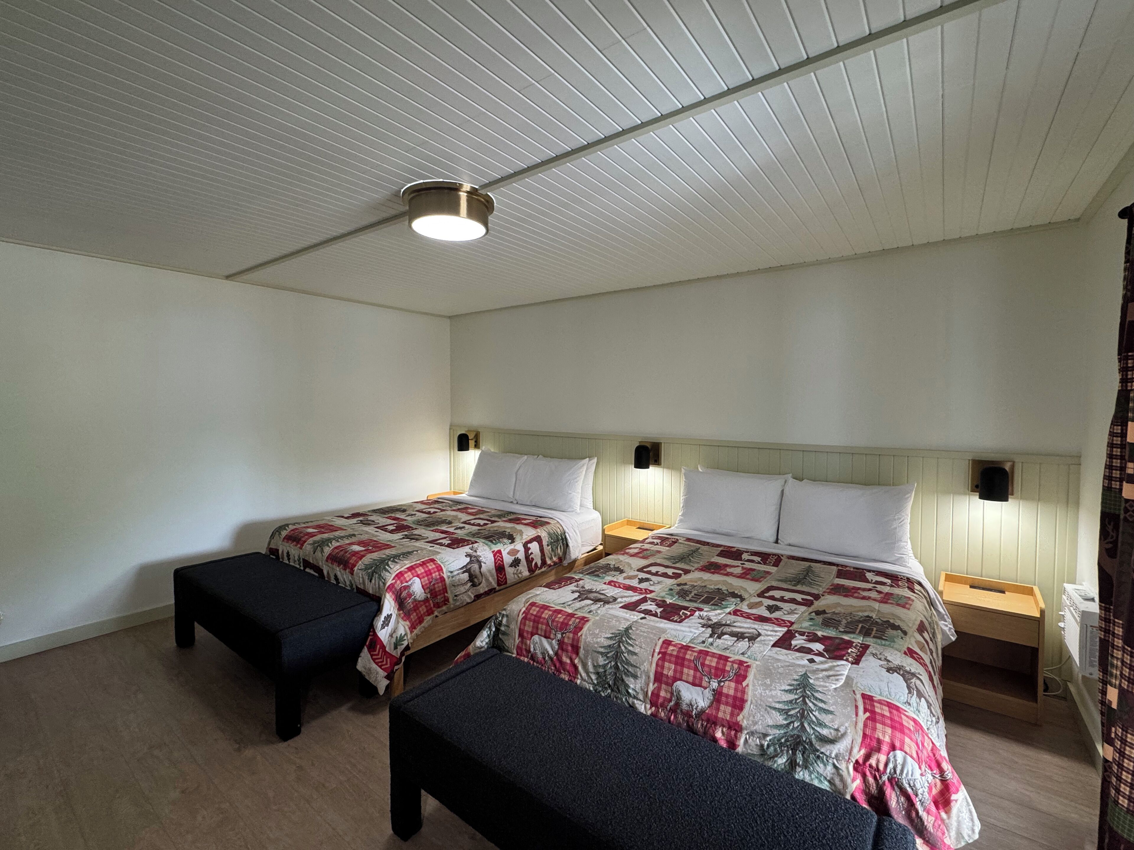 Una habitación con dos camas, cada una con cabecero, un banco y una mesita de noche.