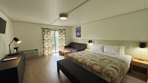 A bedroom with a bed, a bench, a desk with a lamp, a couch, and a window with curtains. - Ski Mountain Lodge (Gatlinburg)