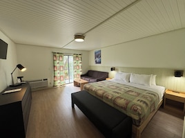 Un dormitorio con cama, una banca, un escritorio con lámpara, un sofá y una ventana con cortinas.