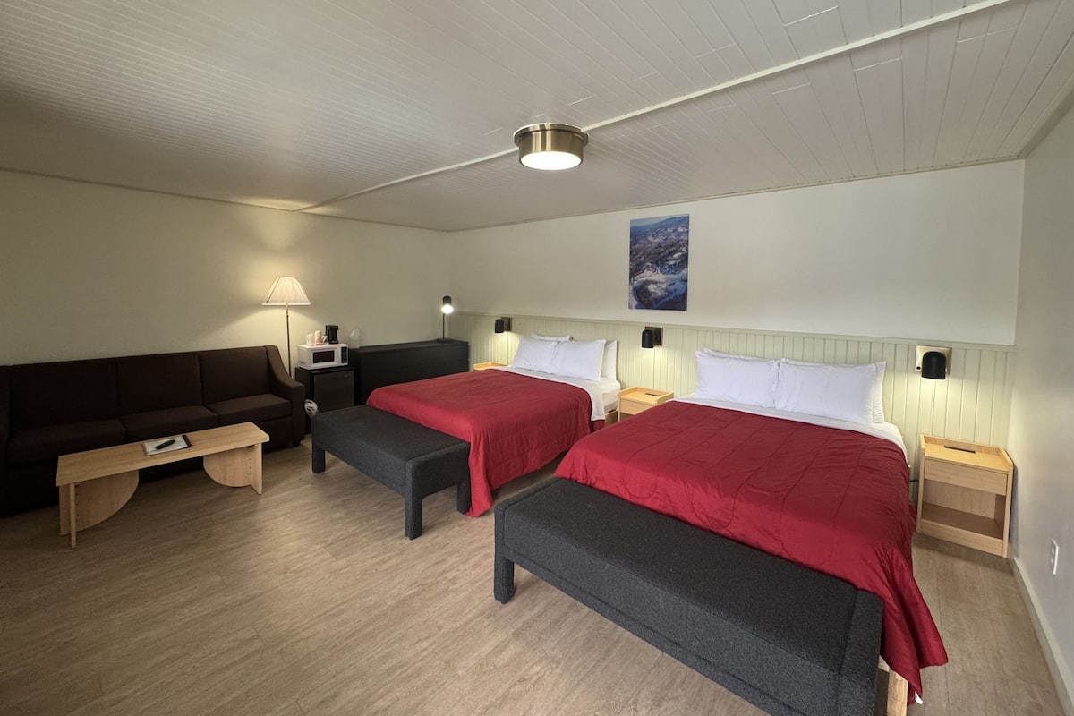 Habitación de hotel con dos camas, un sofá, una mesita y un banco.