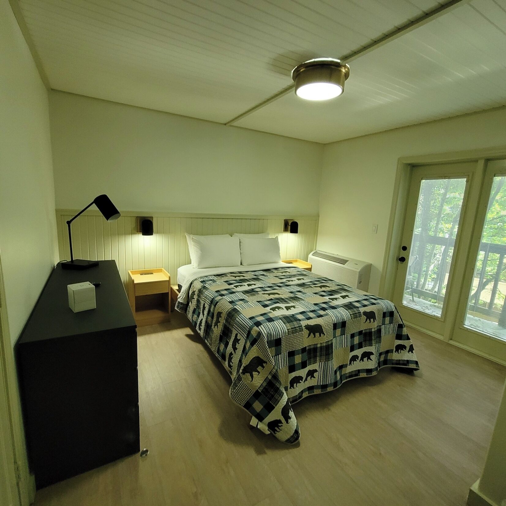 A bedroom with a bed, bedside tables, a desk, and a ceiling light.