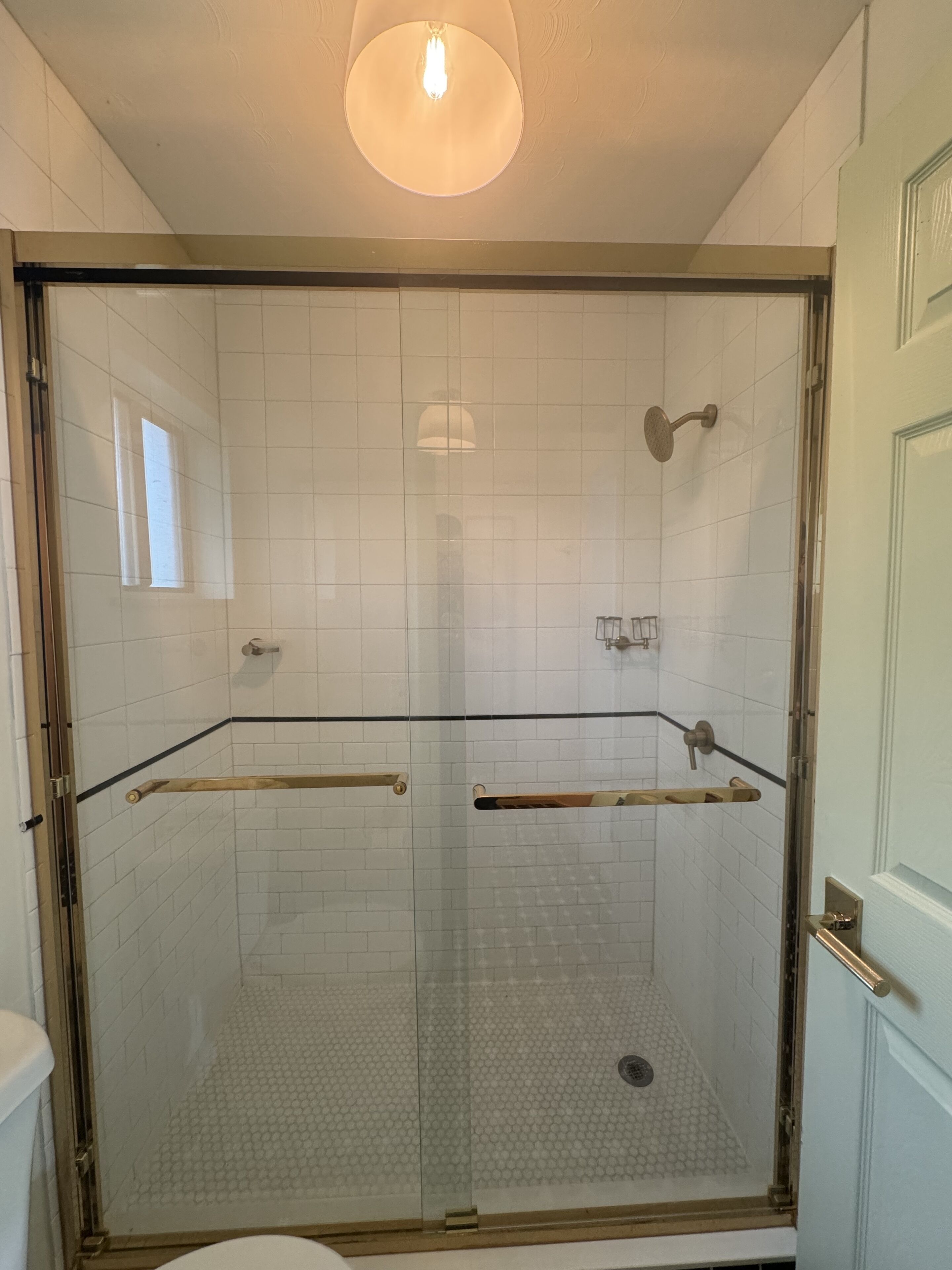 A glass-enclosed shower with a tiled floor, a handheld showerhead, and a handheld shower bar.