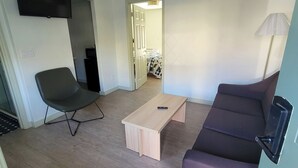 A compact living space with a sofa, a chair, a coffee table, a TV mounted on the wall, and a door leading to another room. - Ski Mountain Lodge (Gatlinburg)