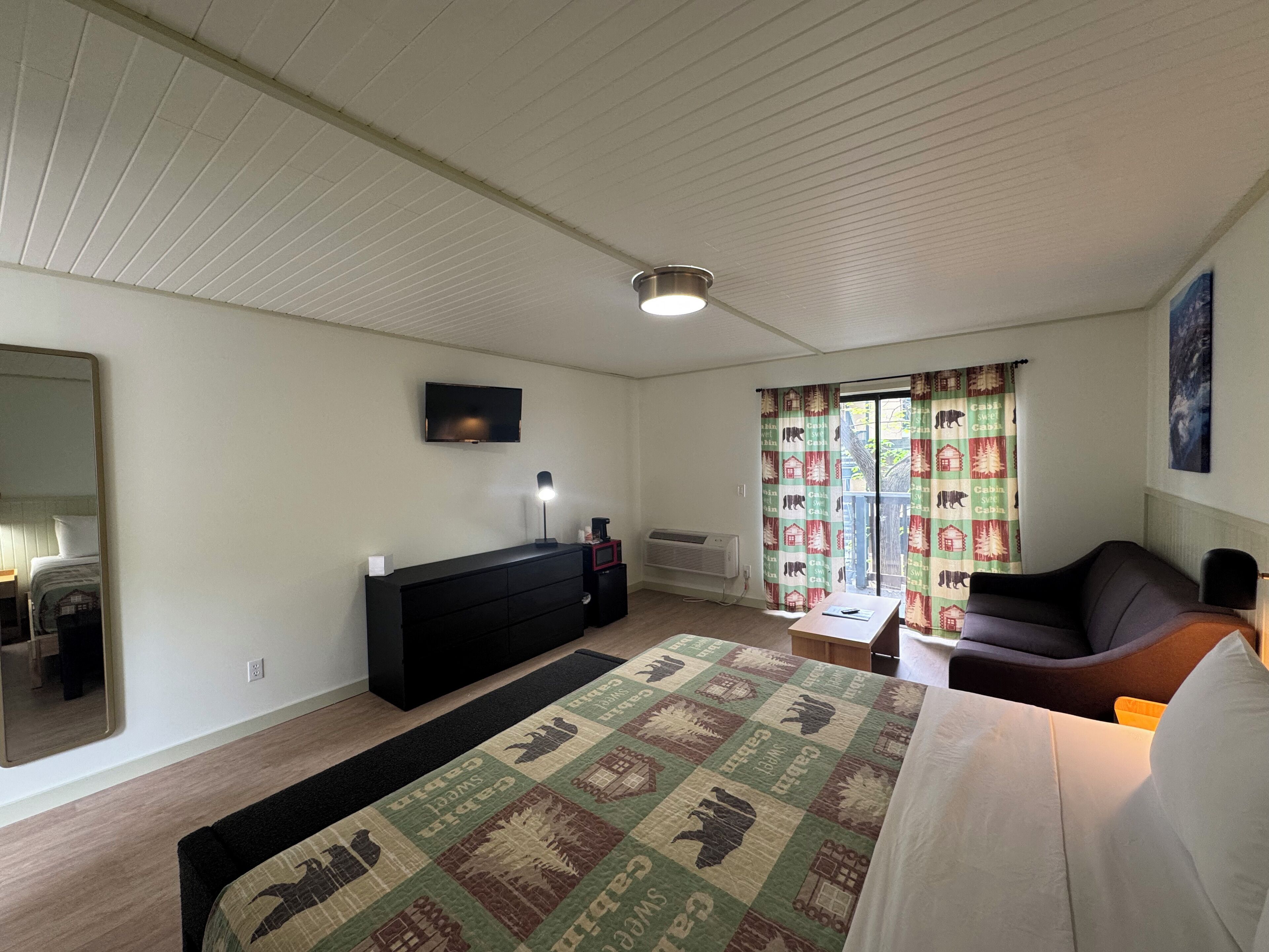 A bedroom with a bed, a dresser, a TV, a window with curtains, and a ceiling light.