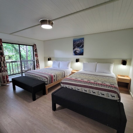 A bedroom with two beds, a large window, and a ceiling light.