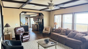 A living room with a sofa, armchair, and coffee table. There is a kitchen in the background with a refrigerator and cabinets. - Lakefront Gem for Family/Fishermen Getaway - 1 Hour from Dallas (Bonham)