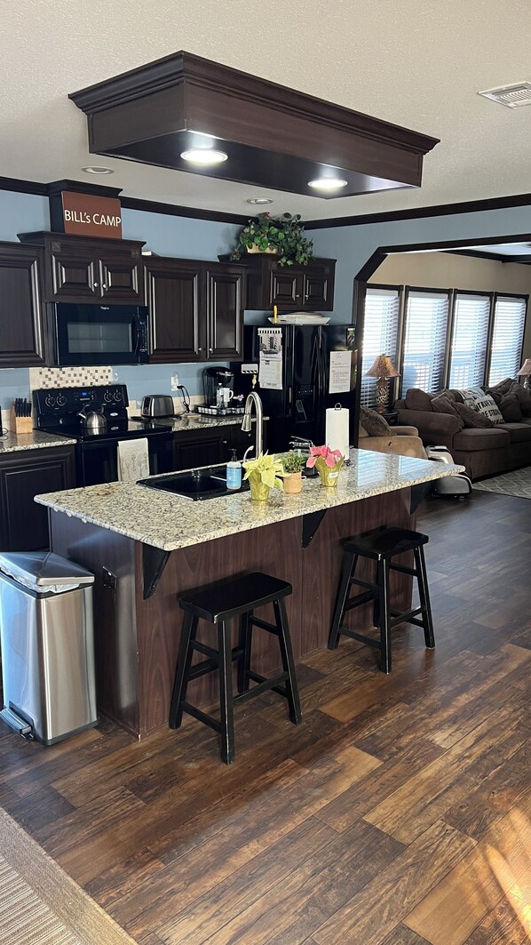 A modern kitchen with dark wood cabinets, a large island with stools, stainless steel appliances, and a sign reading "BILL'S CAMP". - Lakefront Gem for Family/Fishermen Getaway - 1 Hour from Dallas (Bonham)