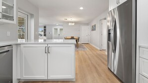 Une cuisine moderne avec des meubles blancs, un réfrigérateur en acier inoxydable et une table à manger en bois.