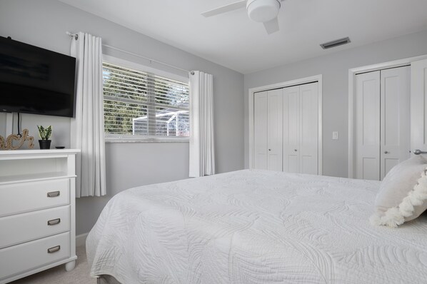 A bedroom with a bed, a TV, a window with curtains, and a ceiling fan.