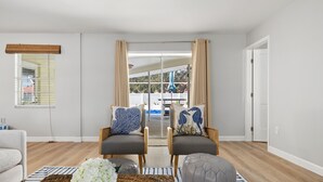 Un salon moderne avec deux fauteuils gris, un canapé blanc et une table basse surmontée d’un tapis tissé.