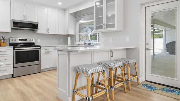 Une cuisine moderne avec des meubles blancs, des appareils en acier inoxydable et un îlot central doté de tabourets de bar.