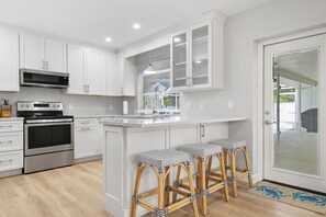 A modern kitchen with white cabinetry, stainless steel appliances, and a central island with bar stools.
