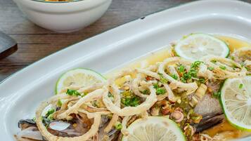 A dish of fish with lime slices and onions on a white plate.