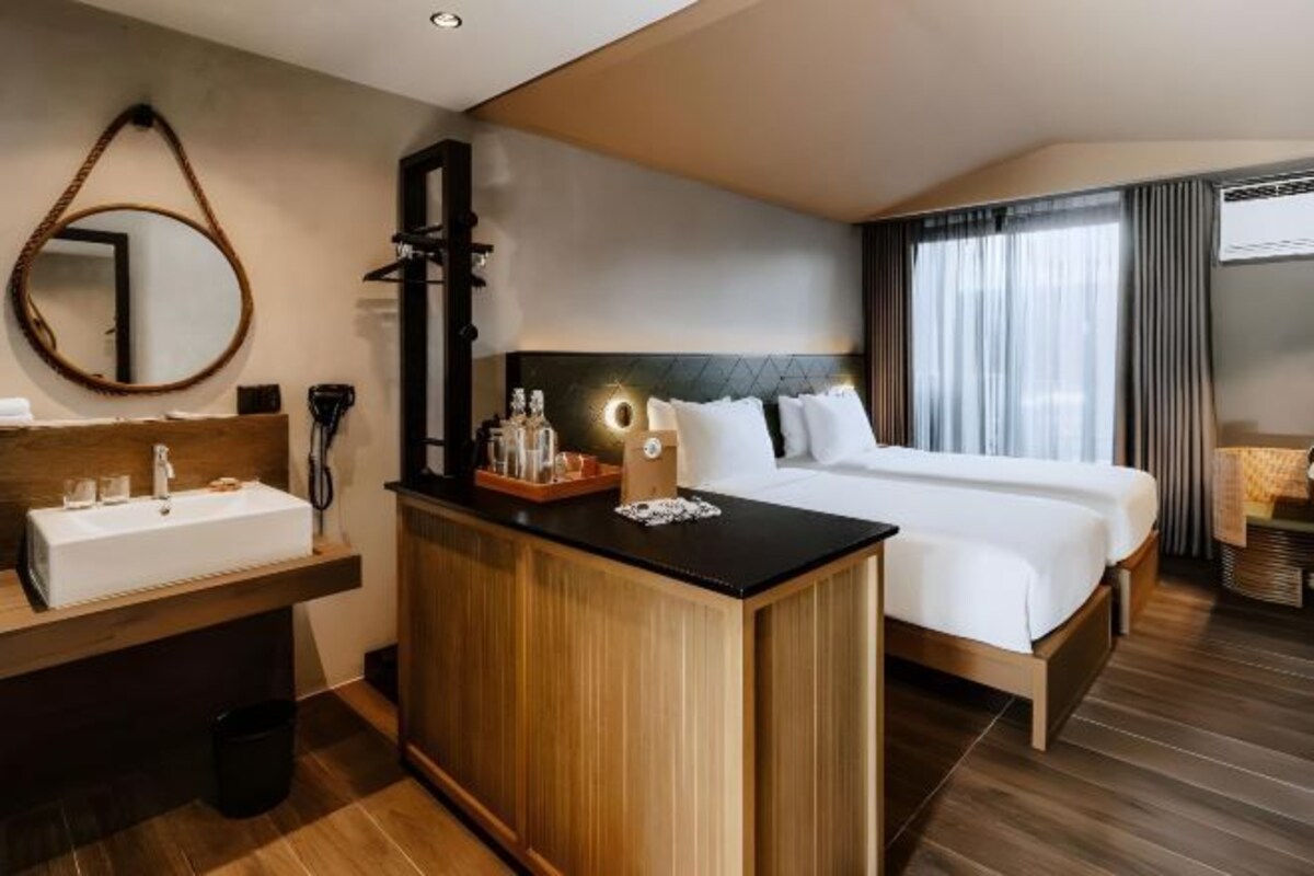 A hotel room with a wooden vanity, a large bed, a round mirror, and a view of the outdoors through a window.