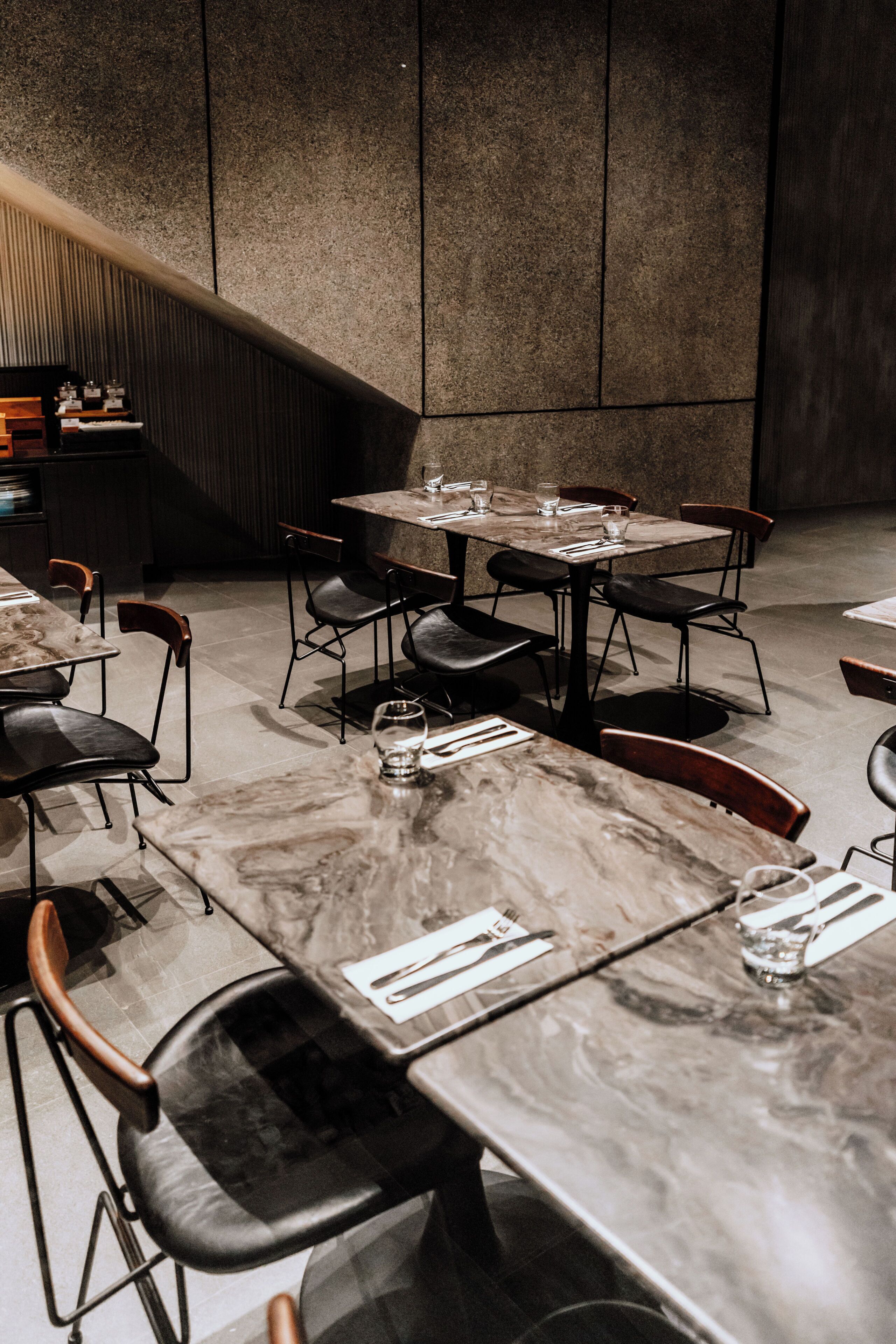 Un comedor moderno con mesas de mármol y sillas de cuero negro, que presenta un diseño limpio y minimalista.