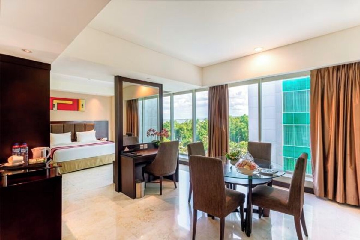 A hotel room with a bed, a desk, a chair, a table, and a large window with curtains.